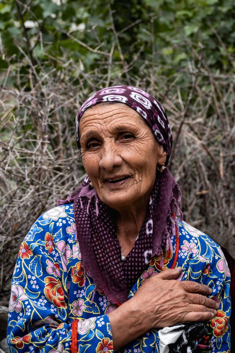 Elderly Tajik woman wearing a floral headscarf sitting outdoors in Wakhan Corridor.