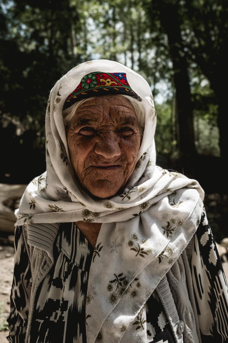 Elderly Tajik woman in traditional ismaeli attire smiling under the bright sun in Ishkashim, Wakhan Corridor.