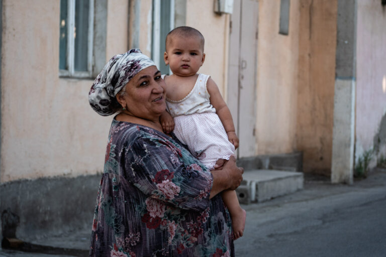 A grandmother holding her child while standing in a narrow alley in Bukhara.