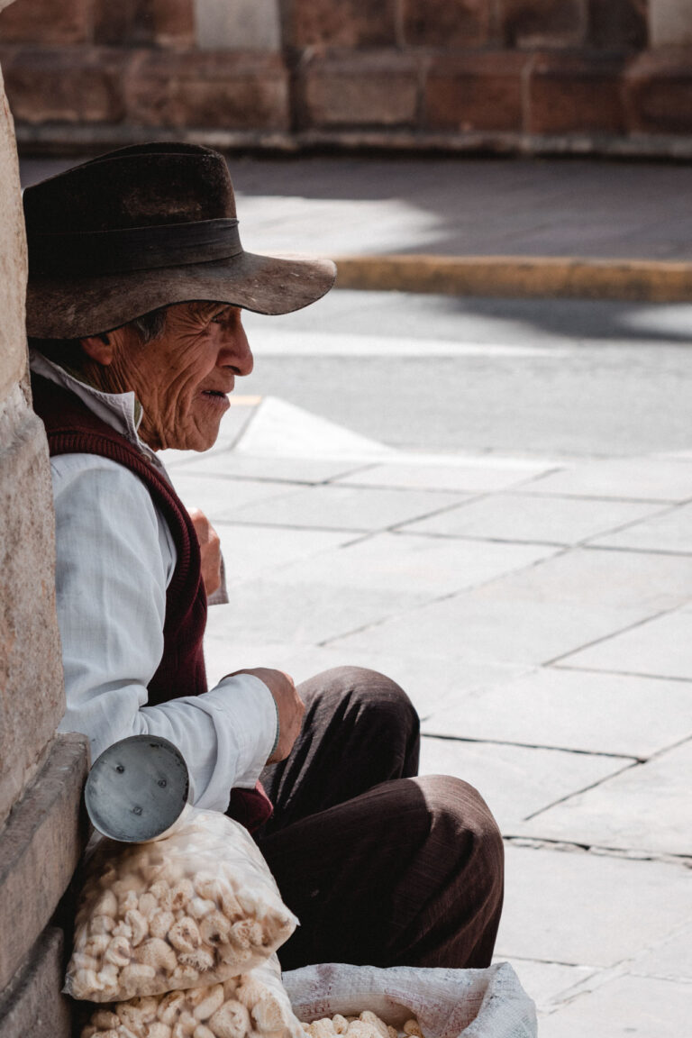 Bolivian man wearing a hat sitting on steps, gazing into the distance.