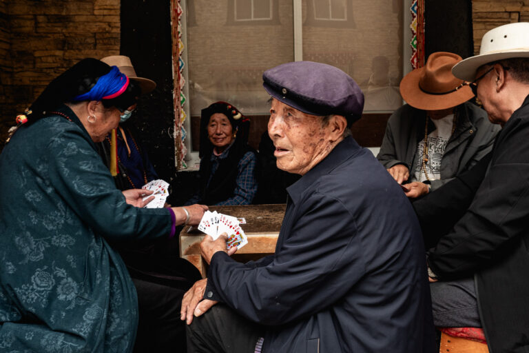 Group of Gyarong women and man in traditional dress playing cards in Danba town.