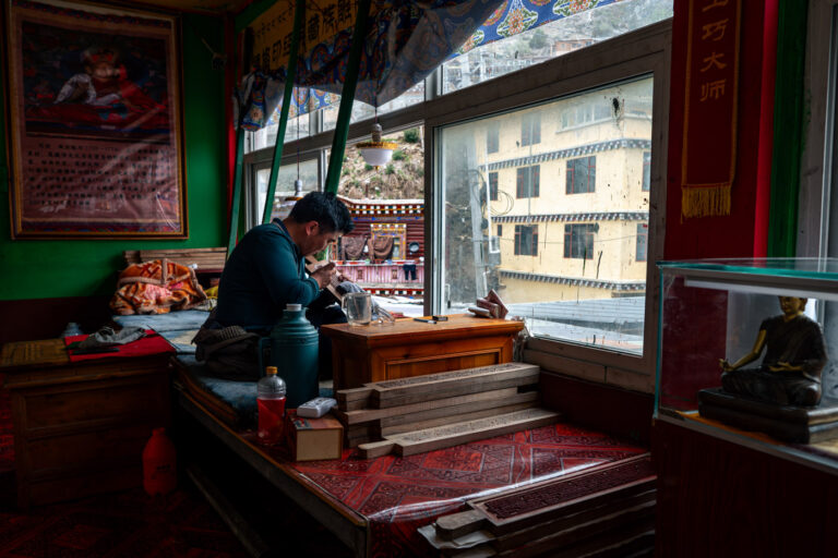 Khampa man in Sichuan Tibet, Dege town, carving Buddhist mantras into wood on train.
