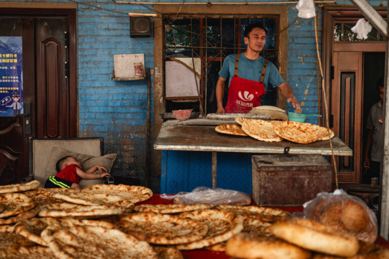Uyghur man and his sleeping child buying bread on the streets of Turpan.