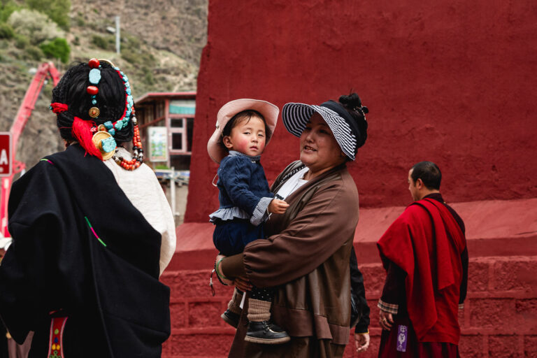 Daily life scene: Khampa mother holding her child outside Dege printing house.
