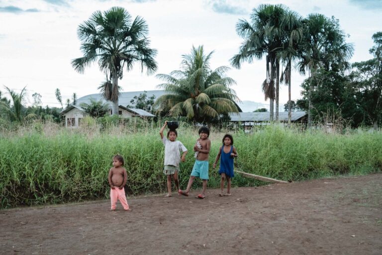 Achuar children playing in a lush Amazonian clearing surrounded by greenery.