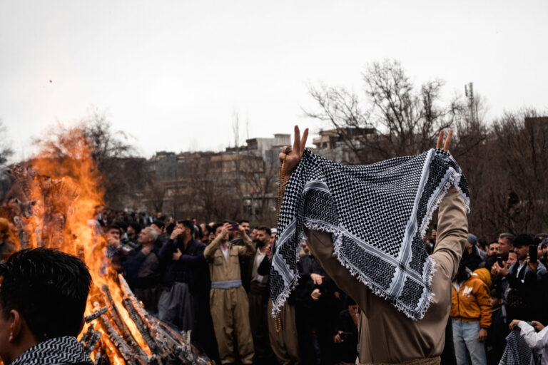 A Kurdish man proudly brandishing his Kurdish scarf in front of a bonfire, symbolizing Nowruz, in vibrant traditional outfits in Kurdistan, Iran