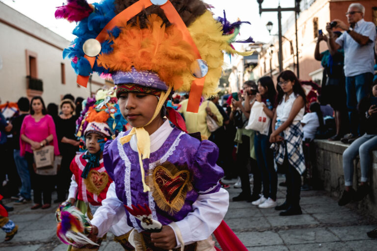 Festive parade scene with colorful costumes and large puppets in Mexico.