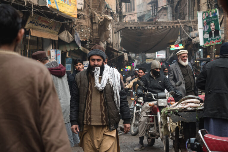 Bustling market street in Peshawar, with vendors and pedestrians filling the frame.