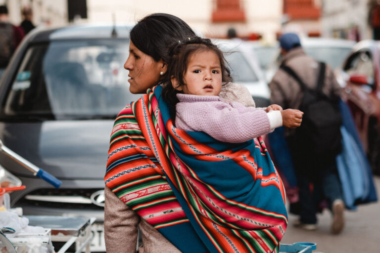 Peruvian woman holding her child wrapped in traditional Andean textiles.