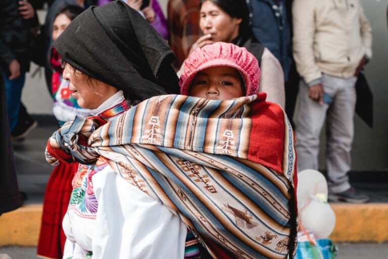 Close-up of an Andean woman carrying her child wrapped in a colorful shawl.