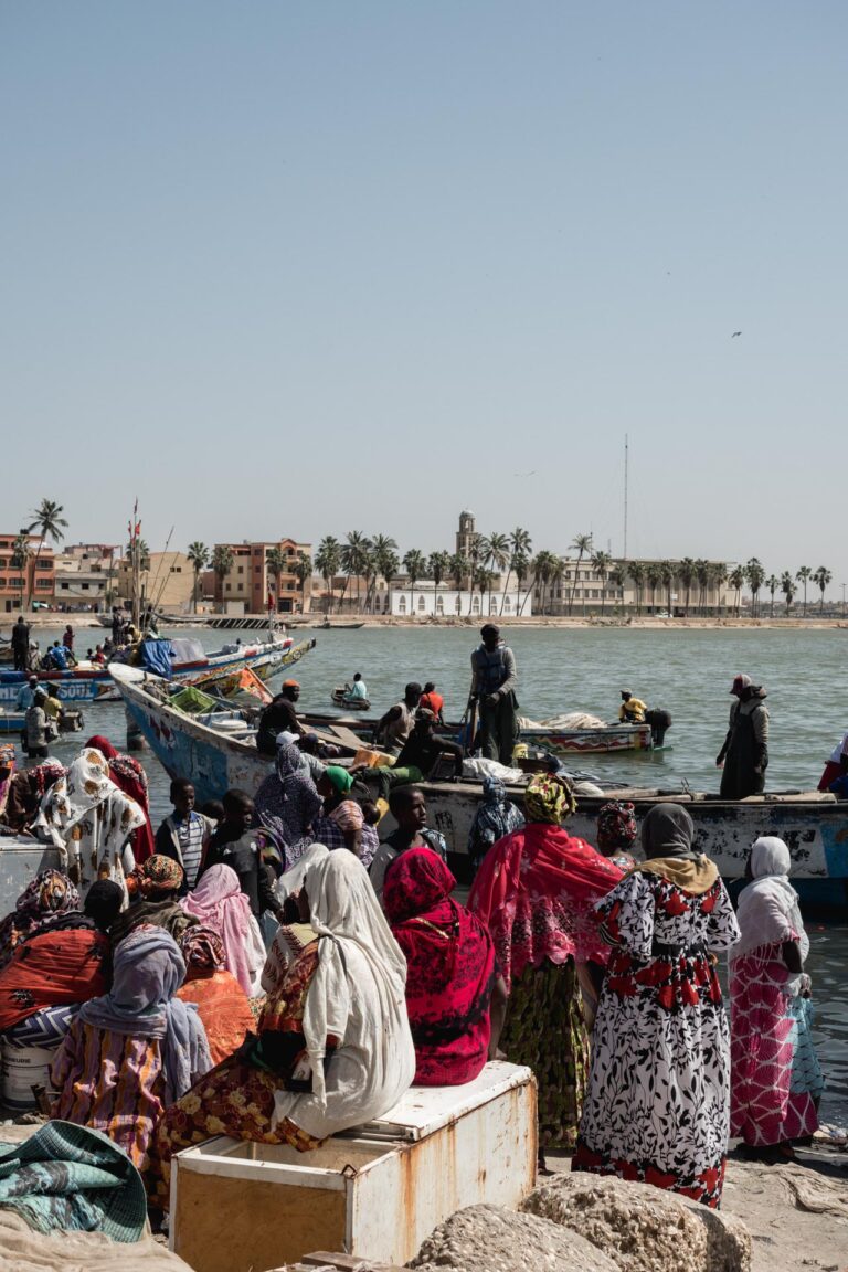 Busy fishing harbor scene with women and children near colorful fishing boats in Saint Louis.