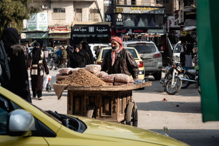 A street vendor in Idlib sells bread, surrounded by traffic and market activity.