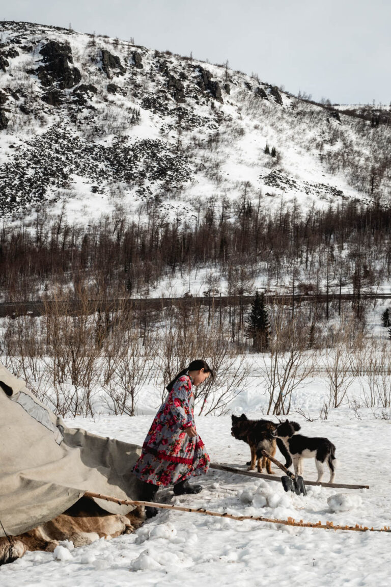 Nenets teenager walking out her chum, vast snow landscape behind.