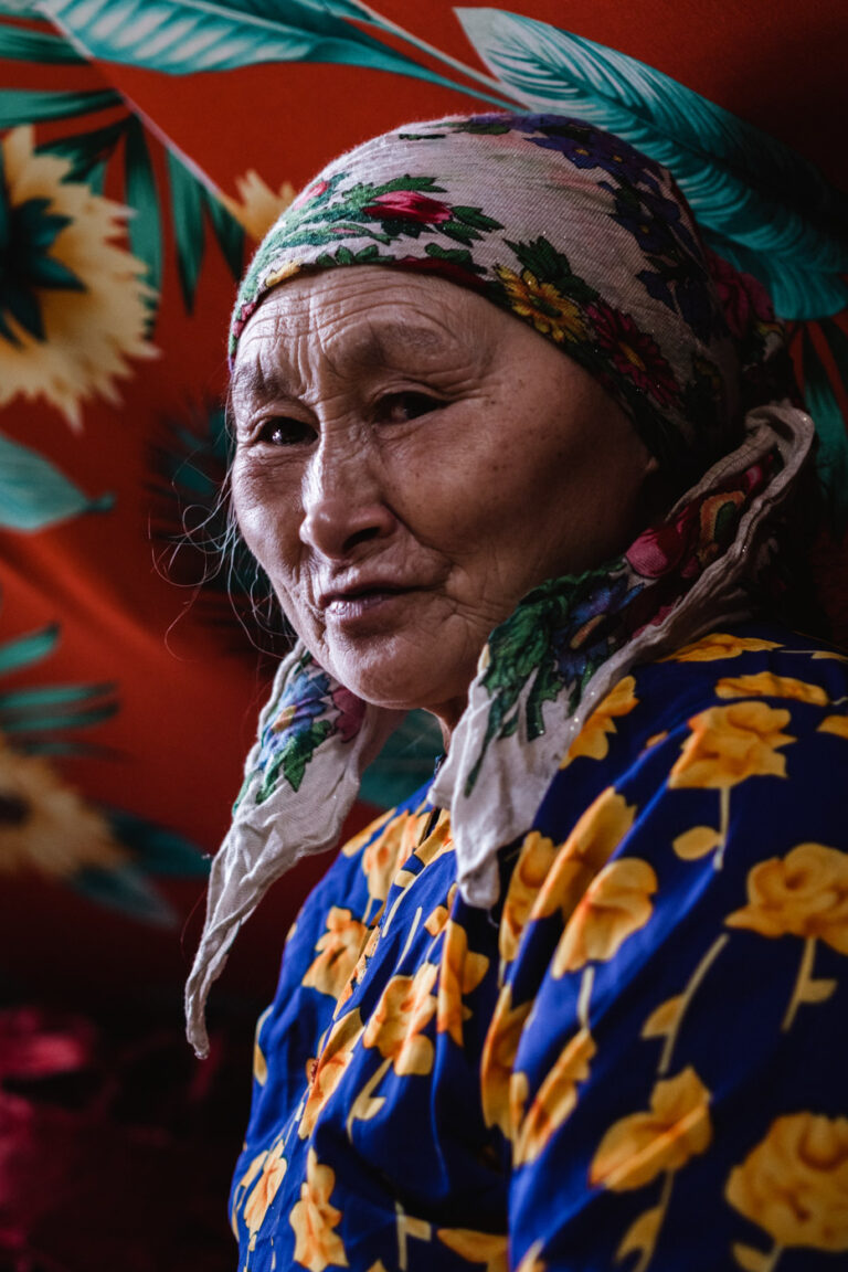 Elderly Nenets woman in colorful traditional dress, eyes closed, peaceful expression.