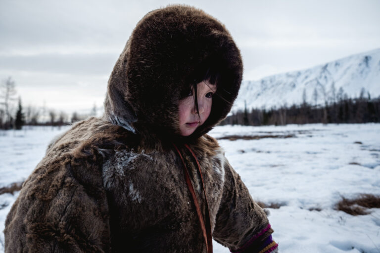 Nenets child bundled in fur coat, standing in deep snow