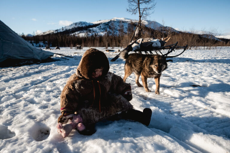 Nenets child riding reindeer with mountain range in background.