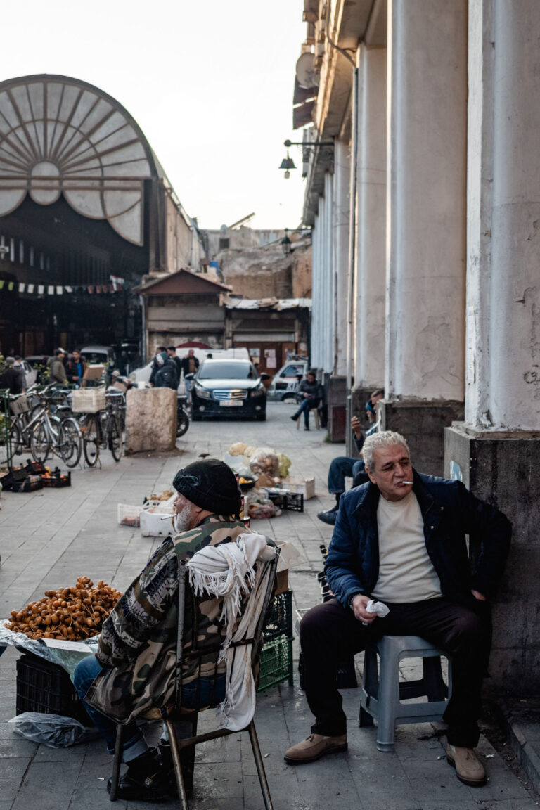 Busy street in Damascus with pedestrians and cars under colorful lights.