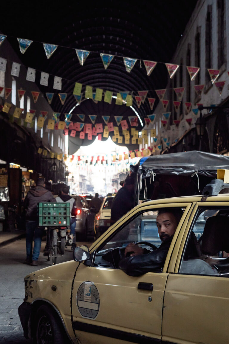 Bearded taxi driver looking through the window of a yellow vehicle in Damascus.