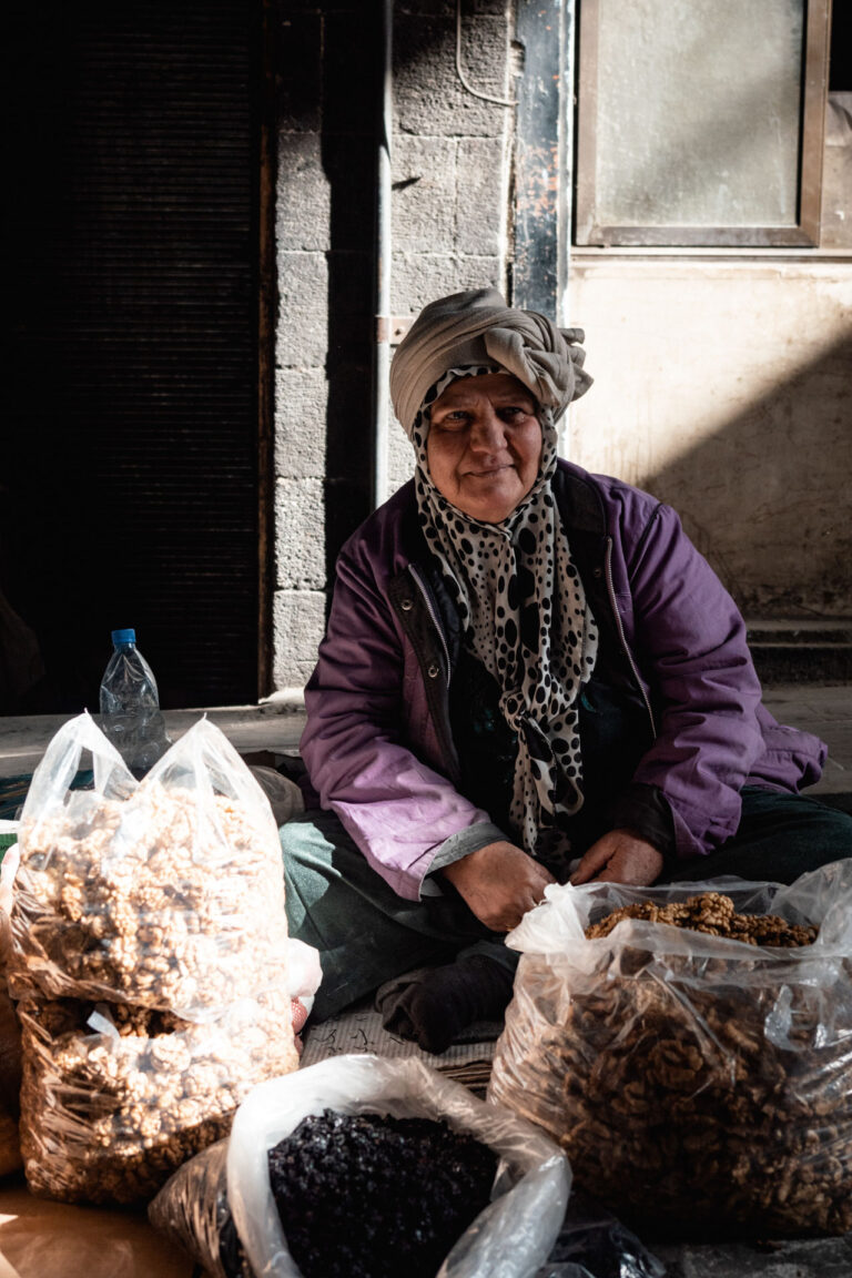 An elderly woman sitting on the floor, selling nuts in the famous Al-Hamidiyah Souq in Damascus.
