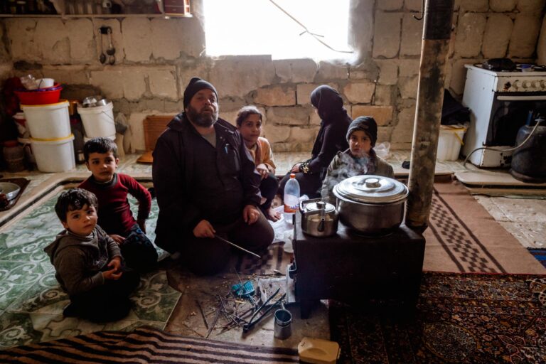 Family sitting inside a dilapidated house, sharing a meal in Saraqib, Syria.