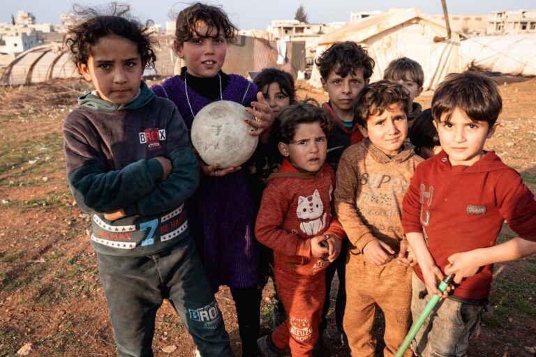 Group of smiling children in a camp or conflict-affected area in Saraqib.