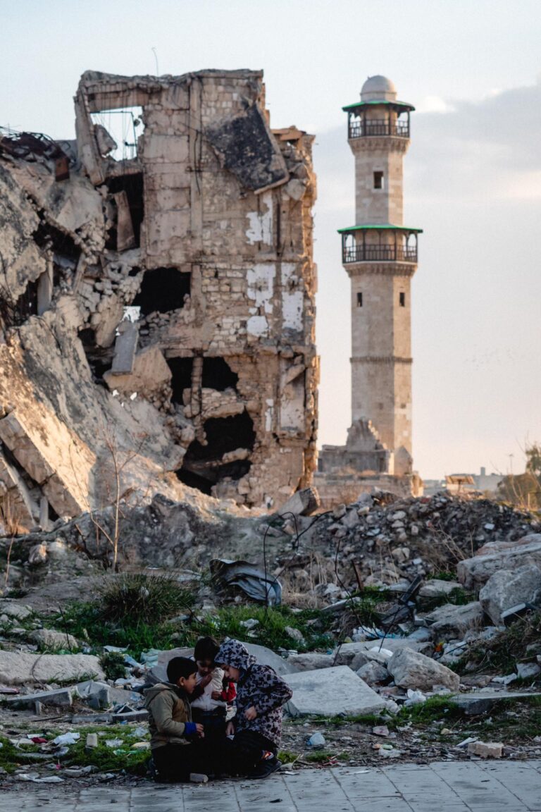 Kids sitting in front of ruins in Aleppo, Syria, symbolizing local resilience.