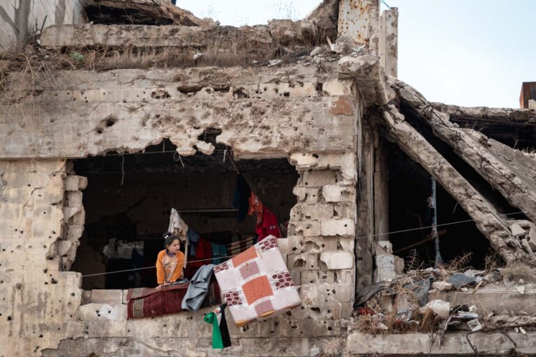Families returned to their destroyed buildings, with clothes hanging inside and a girl looking out at the street from the window in Homs, Syria