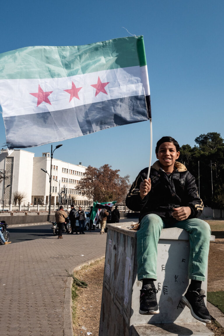 A young boy holding the Syrian opposition flag sits on a concrete barrier in Damascus.