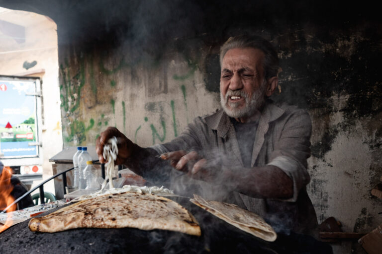 An elderly man bakes traditional Syrian bread in a smoky kitchen in Latakia.