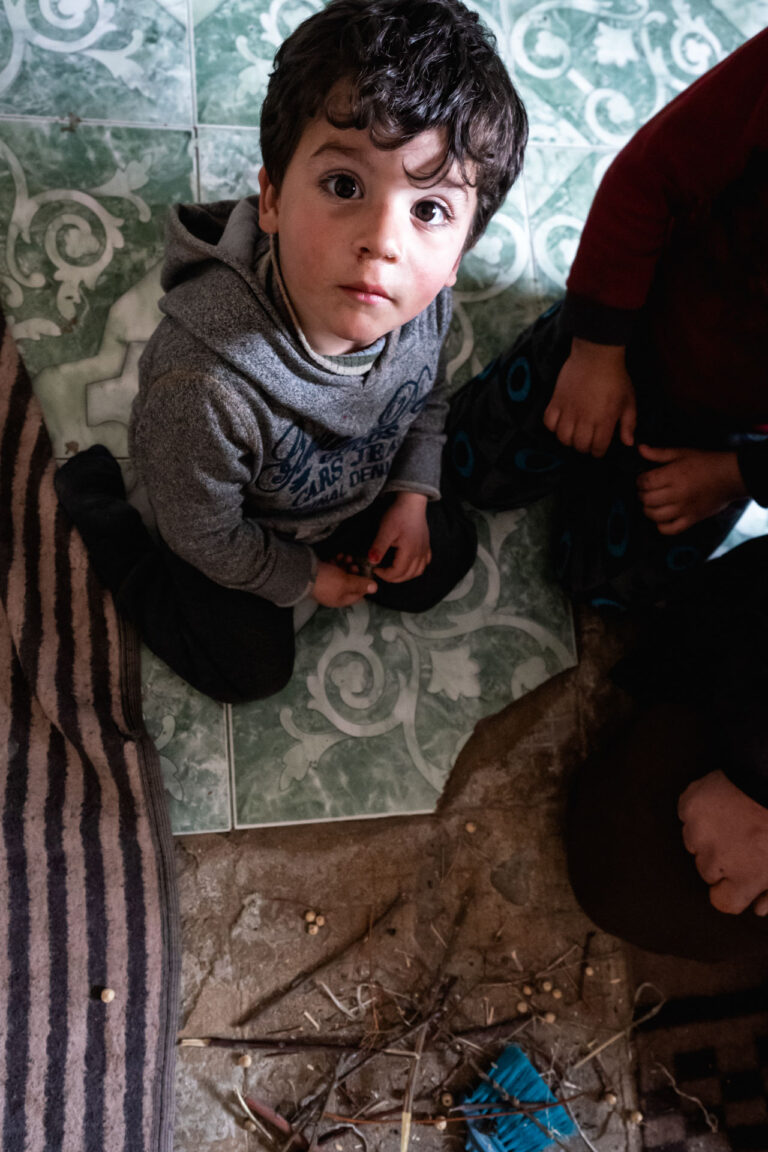 A Syrian child looks up with sadness, sitting on the remaining tiles of his destroyed house.