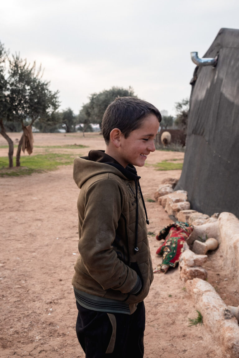 A young boy stands near a refugee tent in Idlib, representing displaced Syrian families.