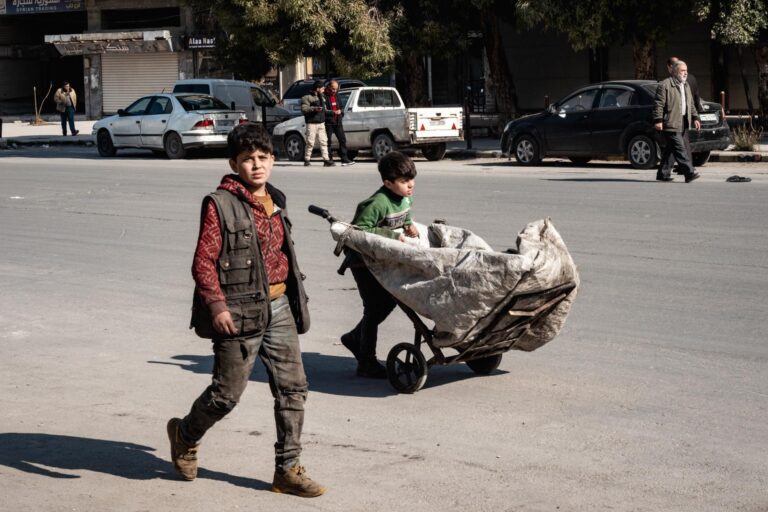A child pulls a cart on a busy street in Aleppo, depicting daily Syrian life.