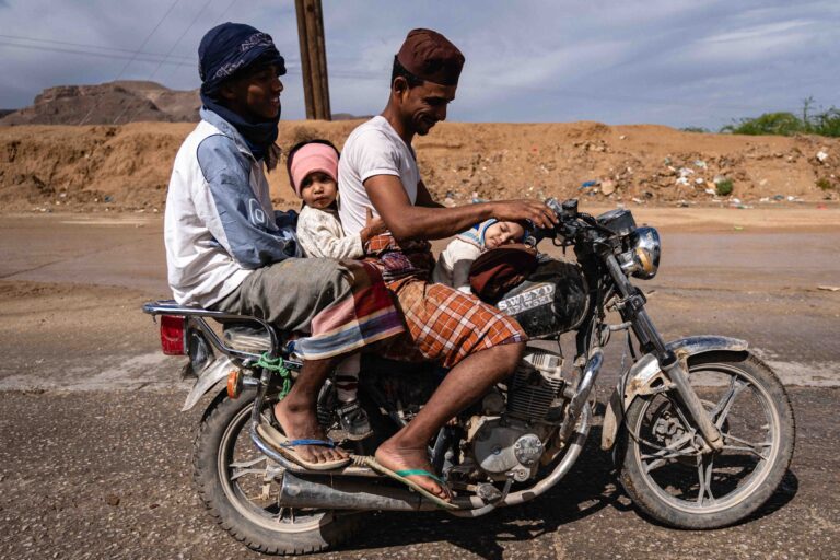 Three people riding a motorcycle through the Hadhramaut region of Yemen.