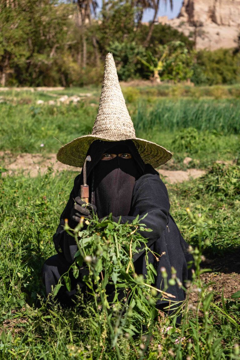 A woman in a traditional black niqab and tall straw hat in Hadhramaut.