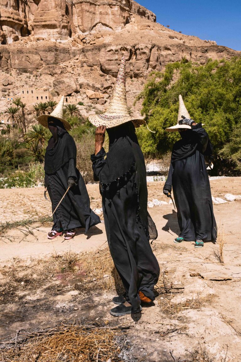 Women in traditional black dress and tall straw hats walking through a rural village.