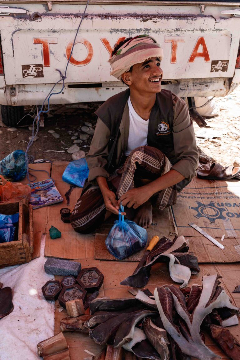 A vendor smiling while sitting in the back of a truck selling goods in Budah.