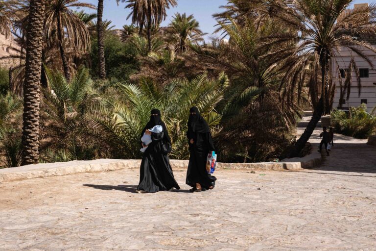 Two women in black niqabs walking through a palm grove in Budah, Yemen.