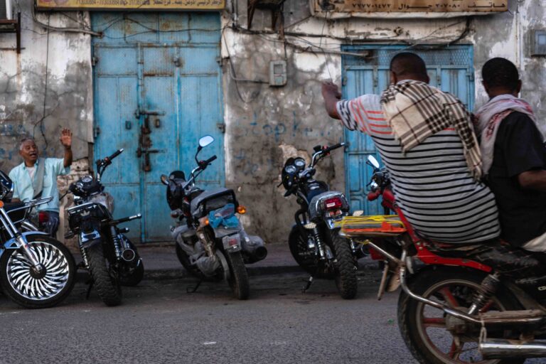 Men sitting on parked motorcycles in a street in Mukallah, Yemen.