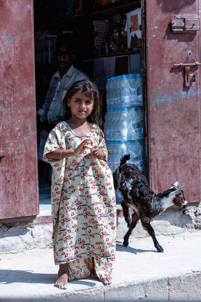 A young girl in a patterned dress standing with a goat in Socotra.