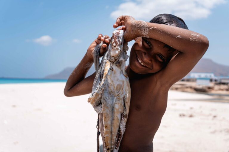 A young boy smiling while holding up a large squid on Delisha Beach.