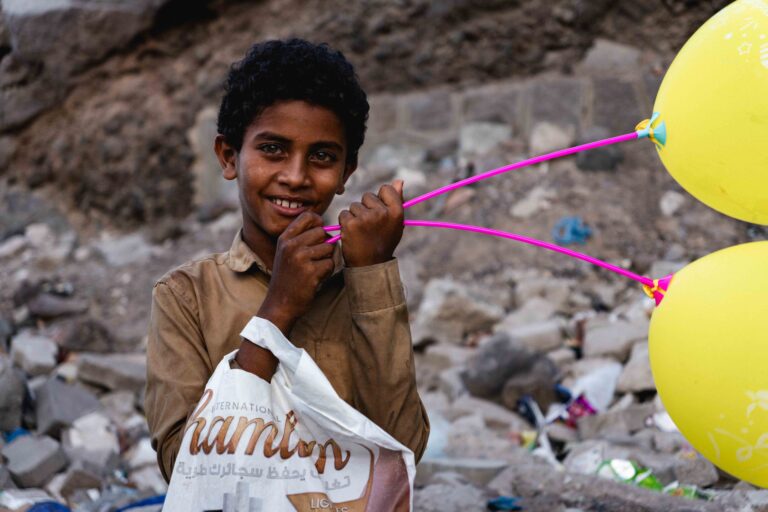 A young boy holding yellow balloons and smiling in a street in Aden.