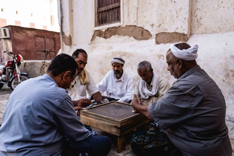 A group of men sitting together outdoors playing a traditional board game in Shibam.