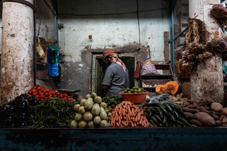A vendor working at a colorful vegetable market stall in Seiyun, Yemen.