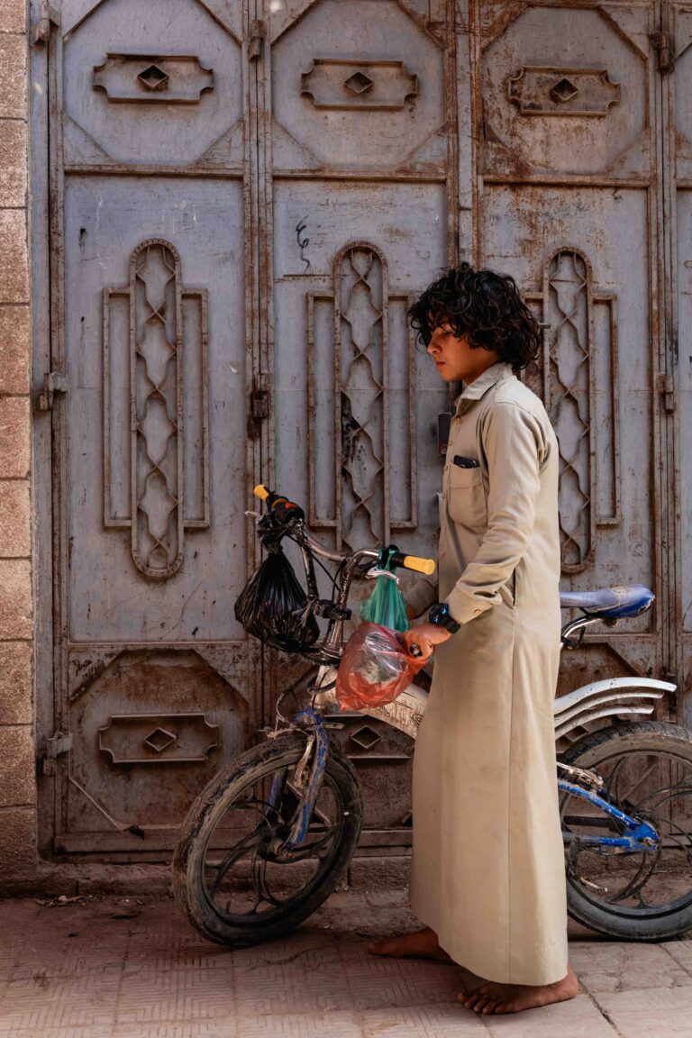 A young person standing with a bicycle in front of an intricate metal door.